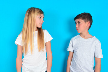 Side view of young happy smiling two kids boy and girl standing over blue studio background
