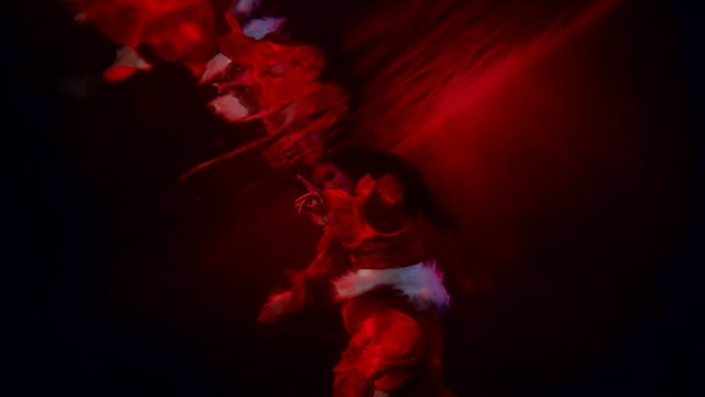 a brunette with long hair dances in dark water and is reflected in the surface. red light. the general plan. the camera is tilted