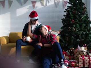 LGBTQ gay couple embracing while sitting in the living room next to Christmas tree. Two homosexual lovers sharing special moments in the morning of Christmas day. - Powered by Adobe