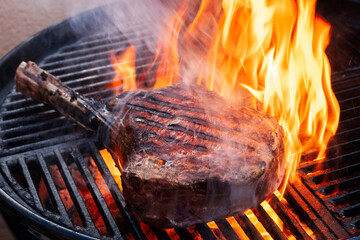 Barbecue dry aged wagyu tomahawk steak offered as close-up on a charcoal grill with fire and smoke