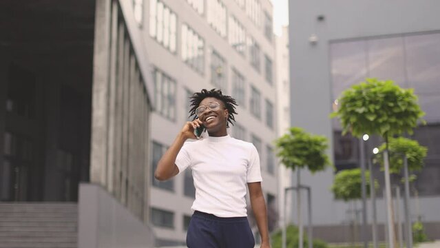 African business woman using smartphone while going outdoors near office building. Concept of technology, work and modern lifestyles. Successful female career.