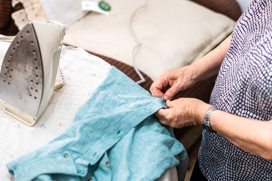 Hands Of Unrecognizable Older Woman Prepares A Blue T-shirt For Ironing