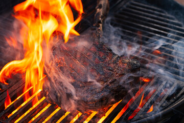 Barbecue dry aged wagyu tomahawk steak offered as close-up on a charcoal grill with fire and smoke