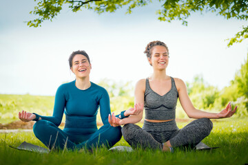 Naklejka na ściany i meble Two lovely friend doing yoga in nature.Smiling girls sitting in lotus position outdoors.