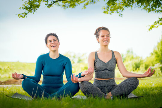 Two lovely friend doing yoga in nature.Smiling girls sitting in lotus position outdoors.
