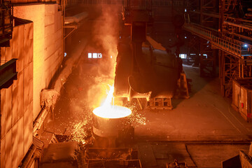 Hot steel pouring from big casting ladle into a mold in an iron foundry.