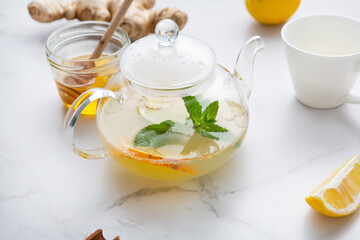 Ginger roots and orange winter tea in glass pot with golden honey on light surface