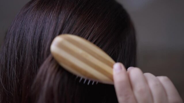 Close-up brunette hair with hand of little woman combing hairdo. Unrecognizable young little person brushing haircut indoors at home
