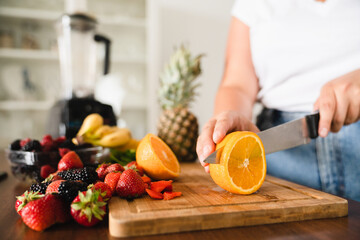 Closeup cropped photo of variety of fruits vegetables on cutting board, while female hands cutting for fruit salad, healthy food. Vegan vegetarian meal