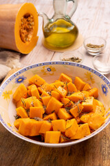 Diced pumpkin pieces in a bowl, with spices and olive oil