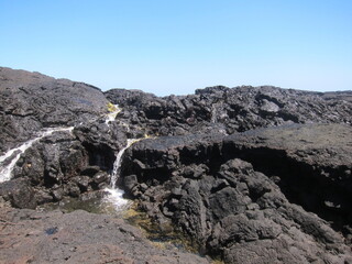 Black volcanic rocks against a clear blue sky. Mini waterfalls. Chalk's Beach at Hilo, Big Island of Hawaii.