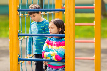 Obraz premium Sad and bored girl and boy stand among the yellow colorful playground, in the park