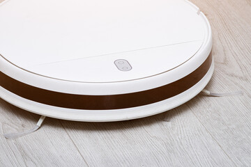 A white modern robot vacuum cleaner hoovers the laminate surface in the bedroom. Modern technologies at home