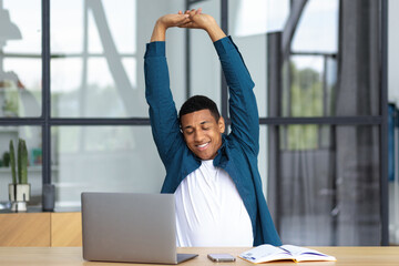 Young African American businessman man working, sitting at the workplace in the office stretching...