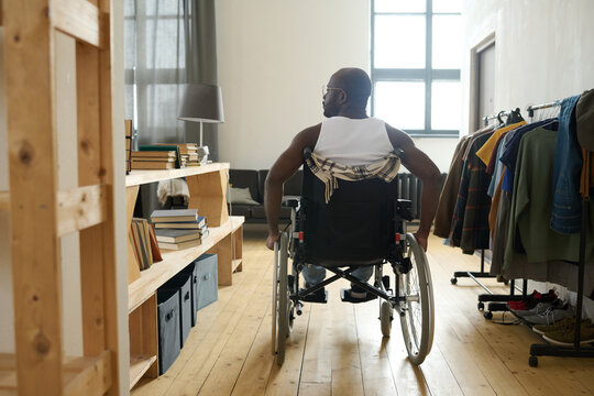 Rear View Of African Man With Disability Riding Along The Room On His Wheelchair, He Living Alone And Caring About Himself