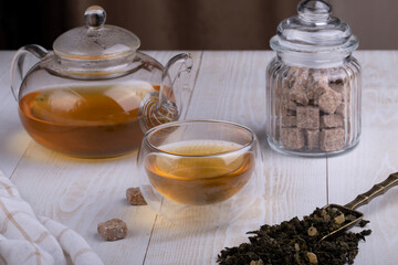 Green oolong tea with fruit in a glass clear cup and glass teapot, brown sugar, close-up, selective focus on the cup