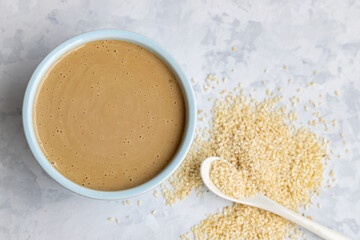 Top down view on traditional oriental sause tahini in a ceramic bowl and sesame seeds on light grey background. Close up. Blurred background.