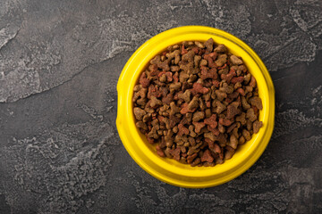 Dry cat food in a yellow bowl on a cement background. Vitamins and nutrients for good health and energy of pets.Copy space.