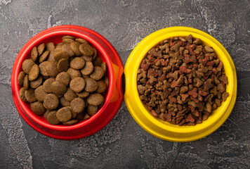 Dry food for cats and dogs in a yellow and red bowl on  cement background.Vitamins and nutrients for good health and pet energy.
