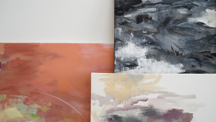 Modern art. Closeup view of three abstract and colorful paintings leaning against the white wall. Beautiful color palette contrast and brushwork texture.