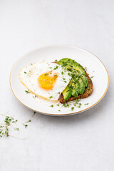 Keto breakfast fried egg, avocado and bread in a white plate. Keto diet concept.