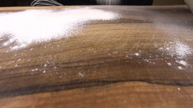 Flour is sifted through a sieve onto a wooden surface.