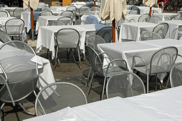 empty chairs and tables with white tablecloth without customers in the alfresco restaurante in the square of European city