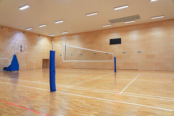 Volleyball net in an empty gym with a mobile basketball hoop in the background