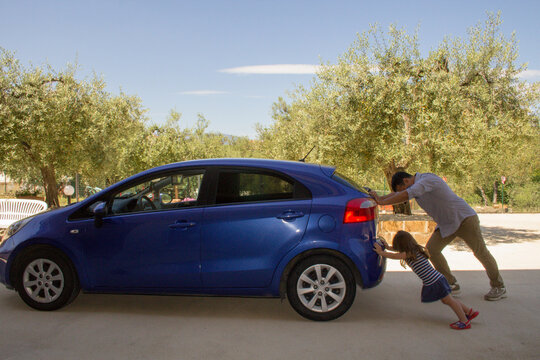 Nice image of a man who with his daughter push their car after having had a breakdown and running out of petrol. Reference to the current expensive fuel