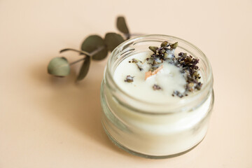 Handmade candle from paraffin and soy wax in glass with wooden wick and dry herbal isolated on pastel beige background. Flat lay, top view, copy space