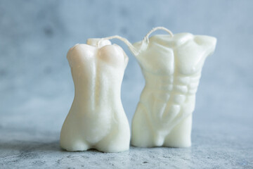Close up of two handmade candles from soy wax in shape man torso and woman body isolated on pastel background.