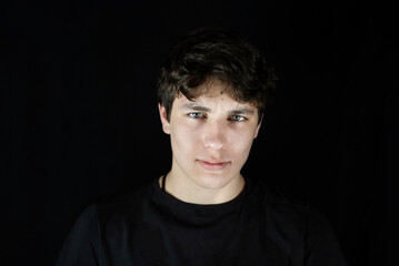 Obraz premium A young man, a teenager with a serious face, sad on a dark background, recent events, world news cause him anxiety, uncertainty about the future