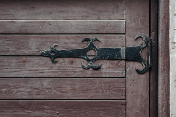 Black openwork forged metal door hinge on a wooden door. Background from dull vintage surface.