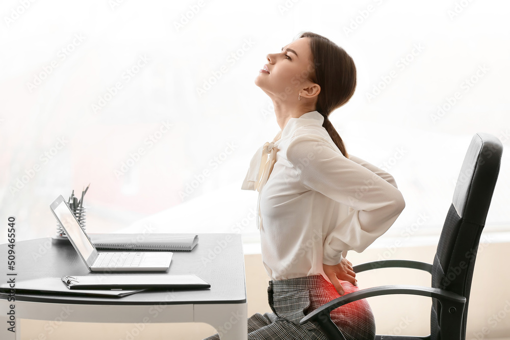 Wall mural Young businesswoman with pain in lower back at workplace