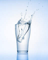 Ice cube falling with splashes into glass water  isolated on white background with copy space