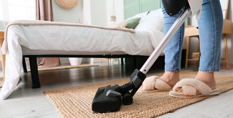 Woman vacuuming wicker rug in bedroom