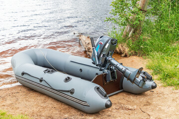 Empty inflatable boat with motor on shore of lake or river. Water transport for hobby or fishing.