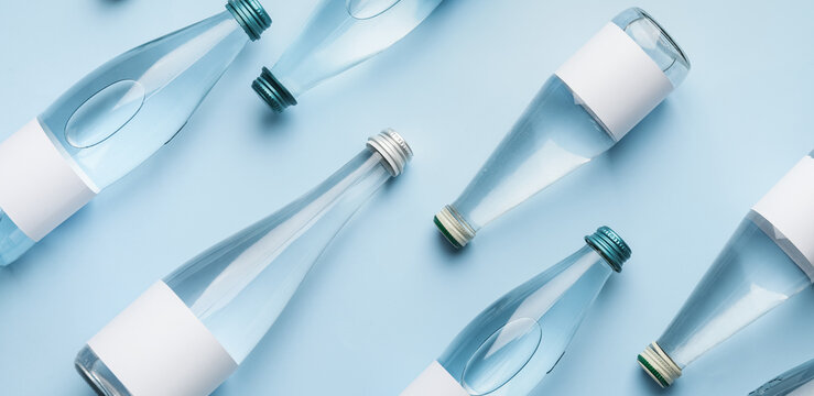 Many bottles of clean water on light blue background, flat lay