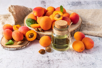 Apricot kernel oil bottle with fresh fruits on wooden tray over stone background.