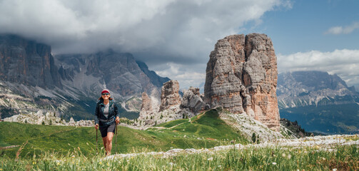 Smiling female trekker walking with backpack and trekking poles by green mountain hill with...