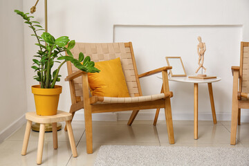 Fototapeta na wymiar Comfortable armchair, houseplant and table near light wall