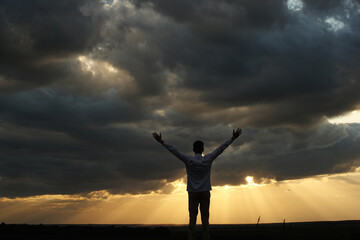 Young man with raised hands silhouette and sunset with dark clouds. Photo was taken 27 May 2022...