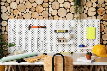 Workplace with pegboards and different tools near wooden wall in workshop