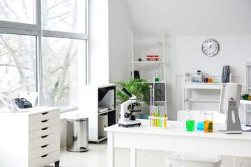 Microscope, tablet computer and chemical glassware on table in medical laboratory