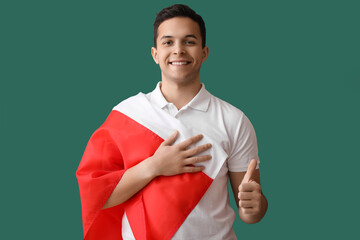 Handsome young man with flag of Poland showing thumb-up on green background