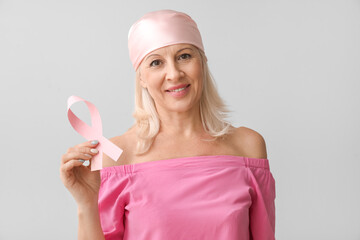 Mature woman with pink ribbon on light background. Breast cancer awareness concept