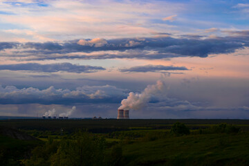 Evening sunset sky scene with dramatic clouds. A nuclear power plant in a field behind a forest