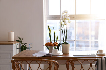 Dining table with delicious breakfast, laptop and orchid flower in light kitchen