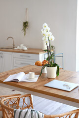 Dining table with delicious breakfast, magazine, laptop and orchid flower in kitchen