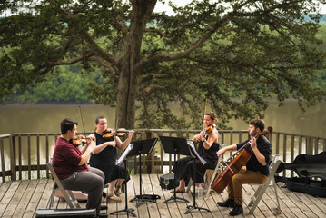String quartet of two young men and two young women playing concert on wooden deck above Missouri...